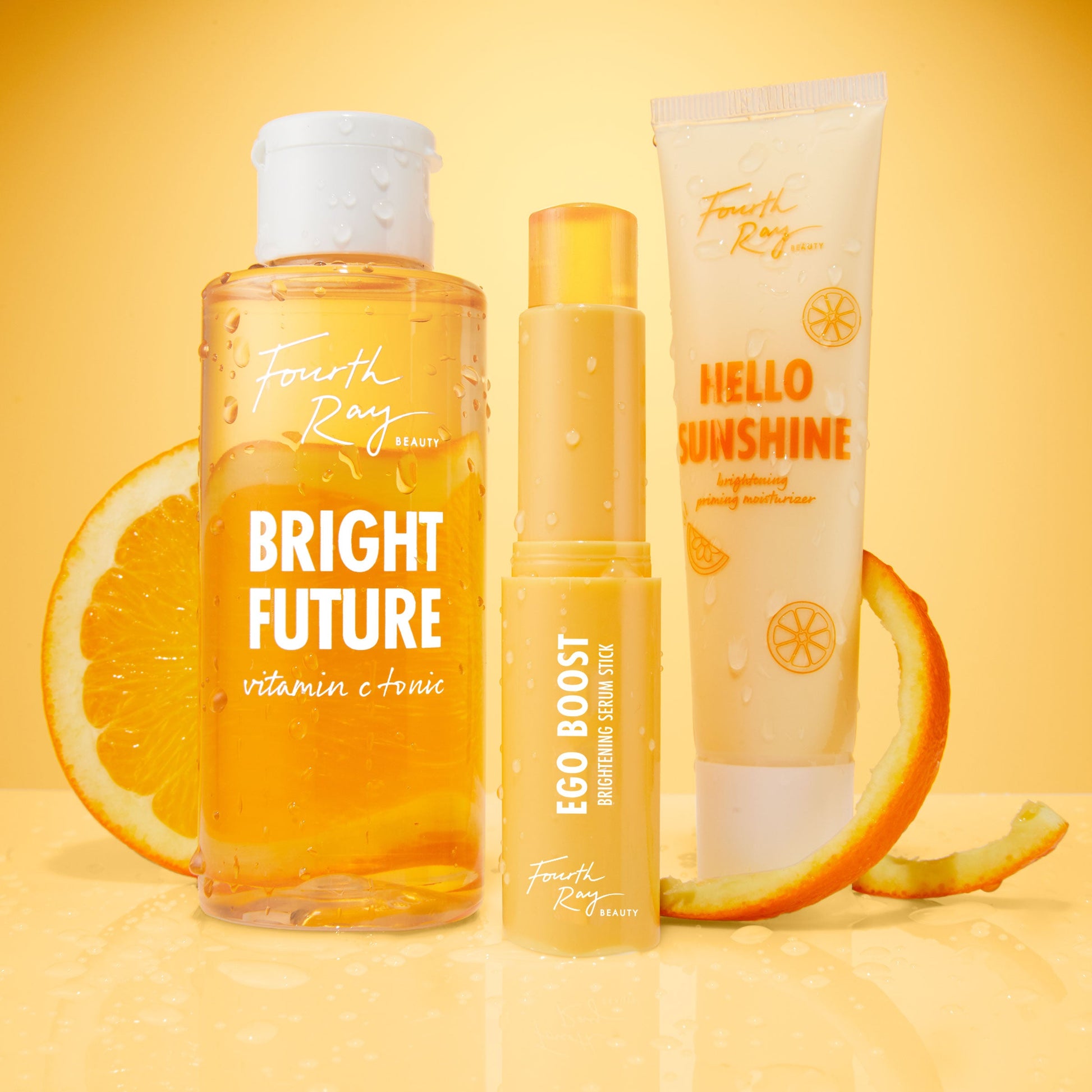 Bright Future Vitamin C Tonic bottle from Fourth Ray Beauty, beaded with water, stands between Ego Boost Brightening Serum Stick and Hello Sunshine moisturizer on a glossy orange surface with citrus slices; ColourPop skincare.